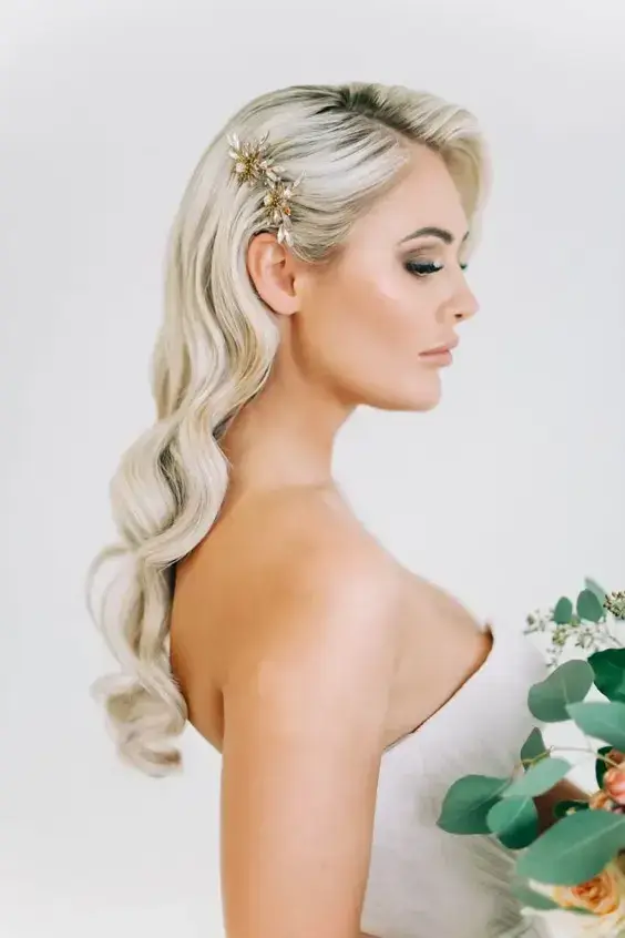 Svadobný účes s kaskádovými vlnami a zlatou ozdobou na boku, vhodný pre elegantný a moderný vzhľad.