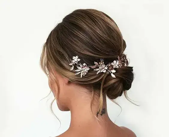 Elegantný polodlhý účes vo forme drdolu, ozdobený kvetinovým doplnkom.