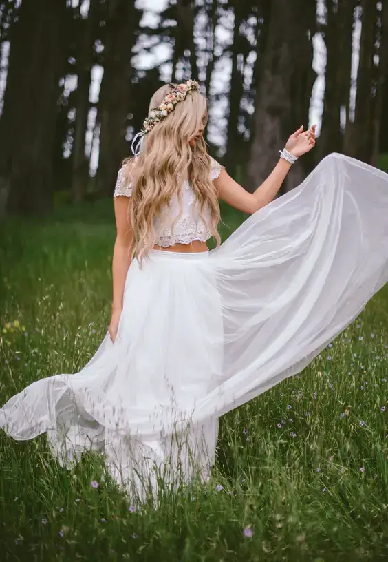 Boho svadobný účes s rozpustenými vlnitými vlasmi a kvetinovým venčekom, doplnený o biele šaty.