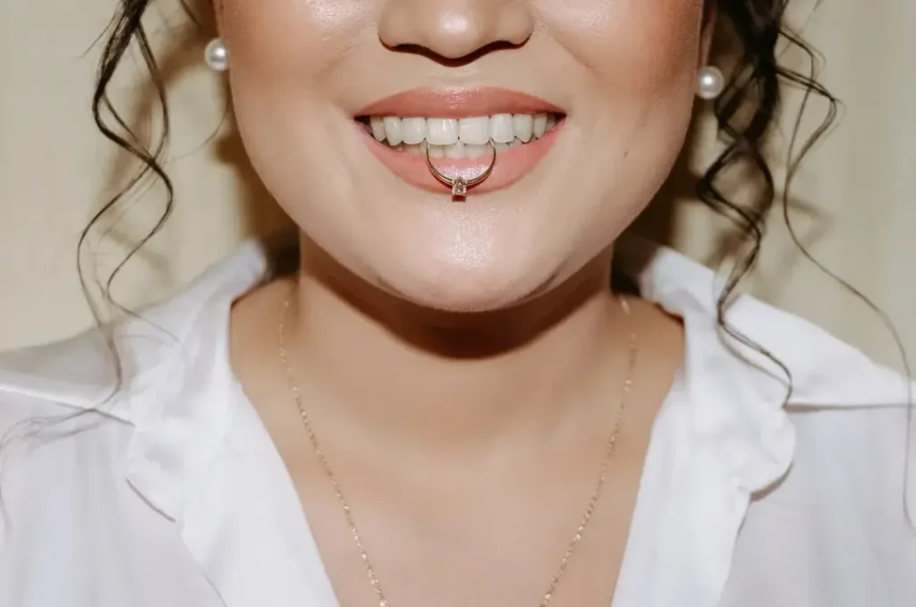 Detailný záber na ústa nevesty, ktorá v zuboch drží zásnubný prsteň.